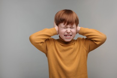 Photo of Hearing problem. Little boy suffering from ear pain on grey background, space for text