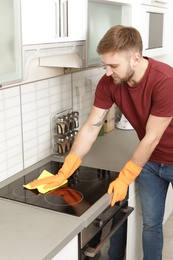 Young man cleaning oven cooktop with rag in kitchen