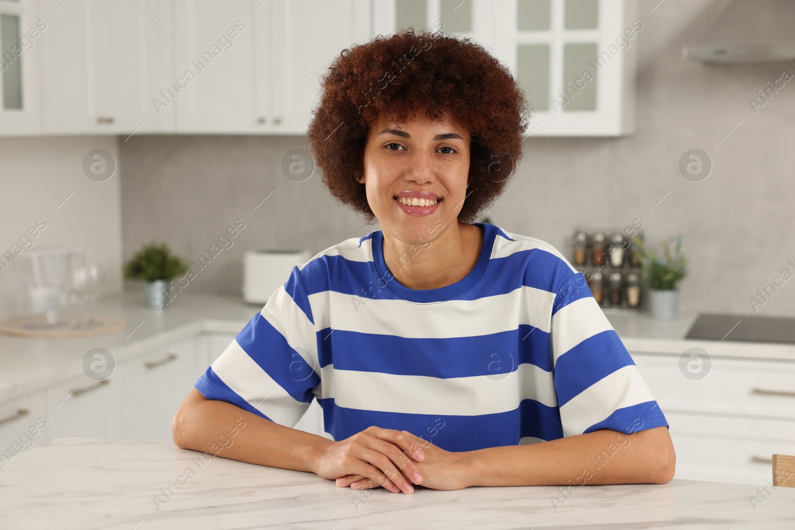 Photo of Happy young woman sitting at table in kitchen