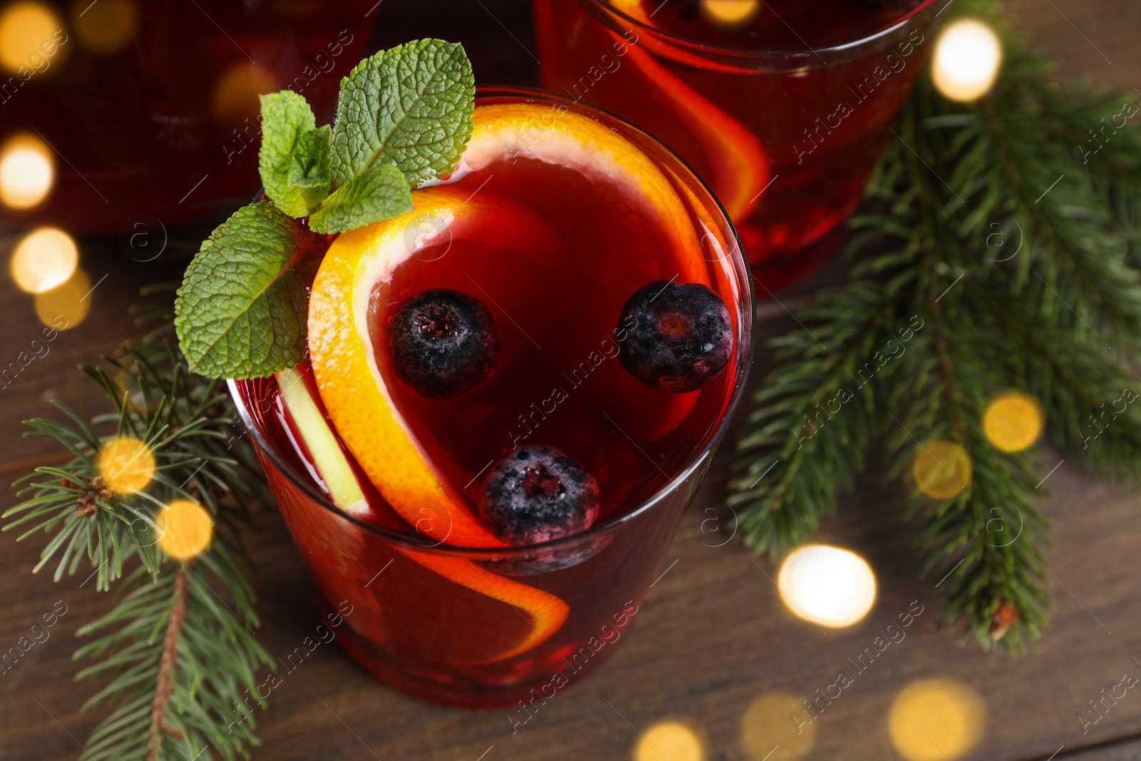 Photo of Aromatic Christmas Sangria drink and fir branches on wooden table, closeup