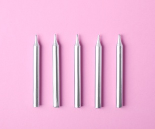 Silver birthday candles on pink background, top view
