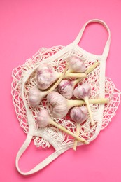 Photo of String bag with garlic heads on bright pink background, top view
