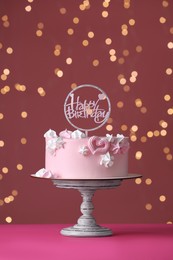 Photo of Beautifully decorated birthday cake on pink table against blurred festive lights