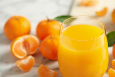 Photo of Glass of fresh tangerine juice and fruits on marble table, closeup