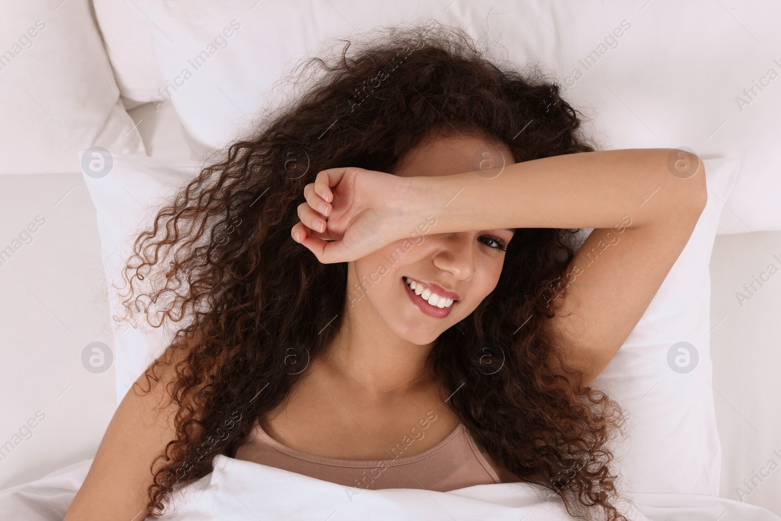 Photo of Happy African American woman awakening in bed, top view