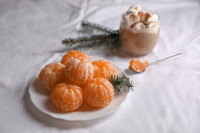 Photo of Peeled delicious ripe tangerines and glass of drink with marshmallows on white bedsheet