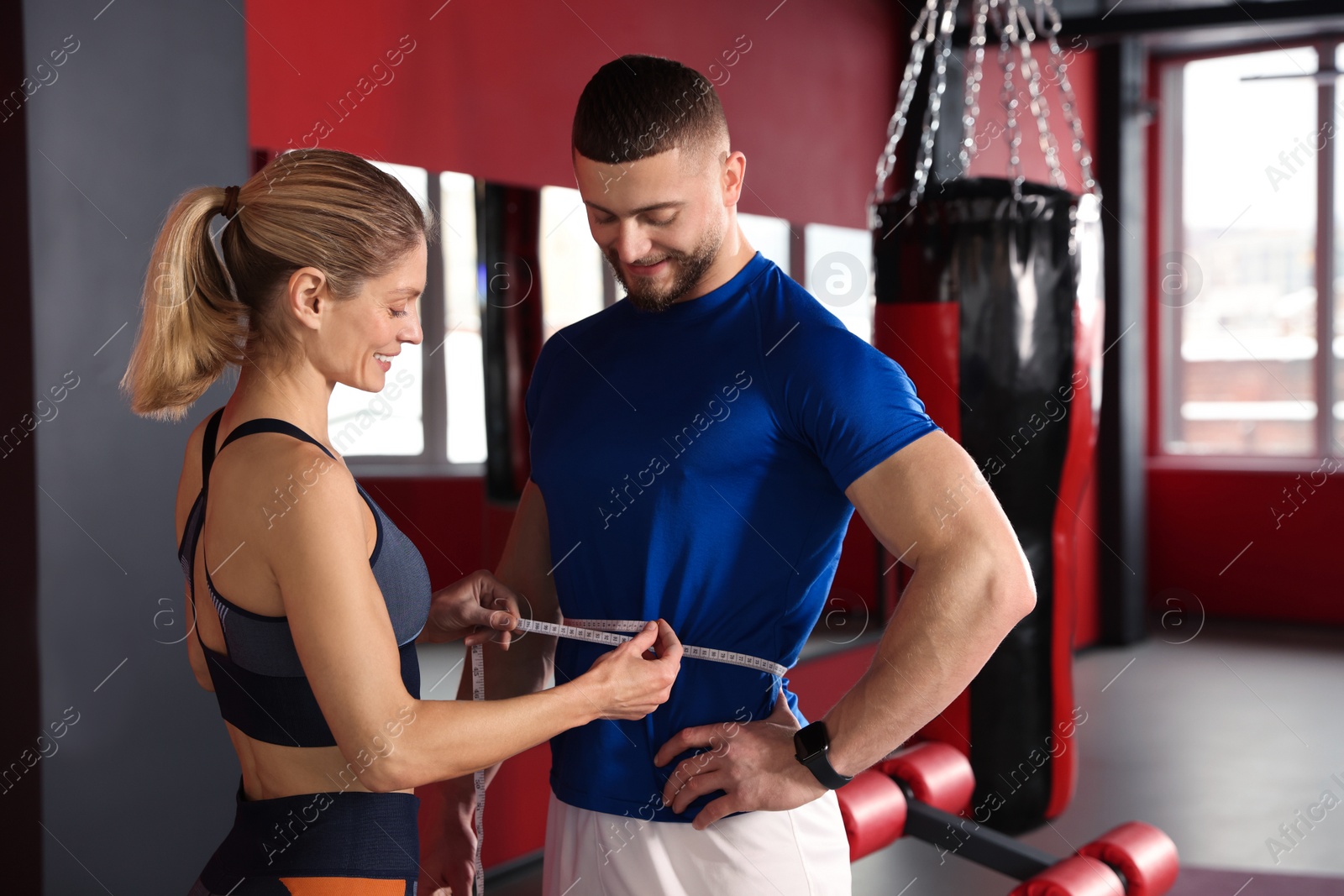 Photo of Trainer measuring man`s waist with tape in gym