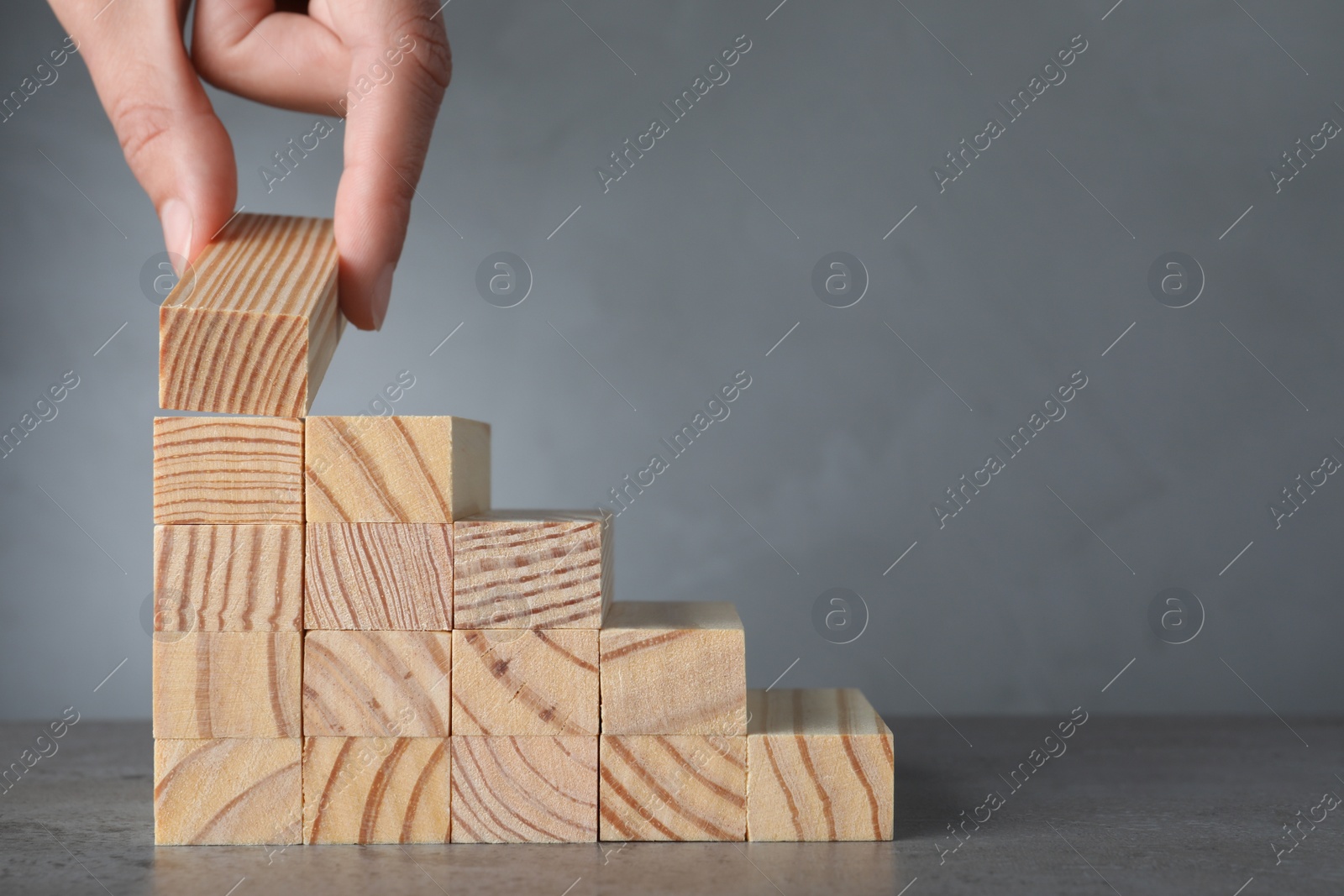 Photo of Closeup view of woman building steps with wooden blocks on grey table, space for text. Career ladder