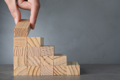 Photo of Closeup view of woman building steps with wooden blocks on grey table, space for text. Career ladder
