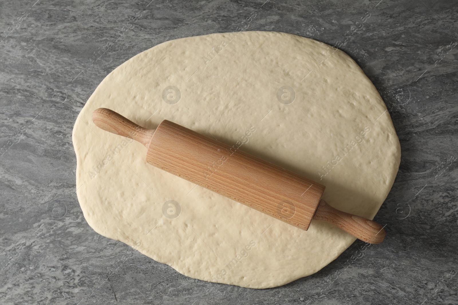 Photo of Raw dough and rolling pin on grey table, top view