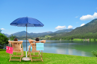 Young couple relaxing on sun loungers near river and mountains. Luxury vacation 