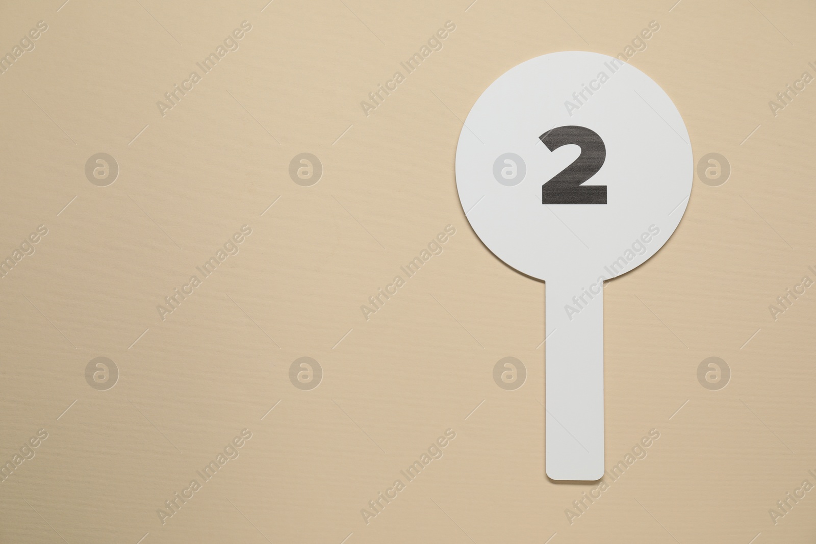 Photo of Auction paddle with number 2 on beige background, top view. Space for text