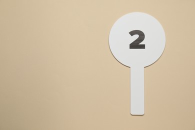 Photo of Auction paddle with number 2 on beige background, top view. Space for text