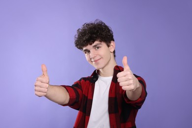 Photo of Portrait of cute teenage boy showing thumbs up on violet background