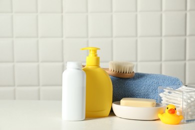 Photo of Baby cosmetic products, bath duck, cotton swabs and towel on white table against tiled wall. Space for text