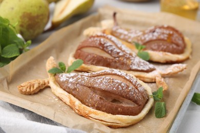 Delicious pears baked in puff pastry with powdered sugar and mint on table, closeup