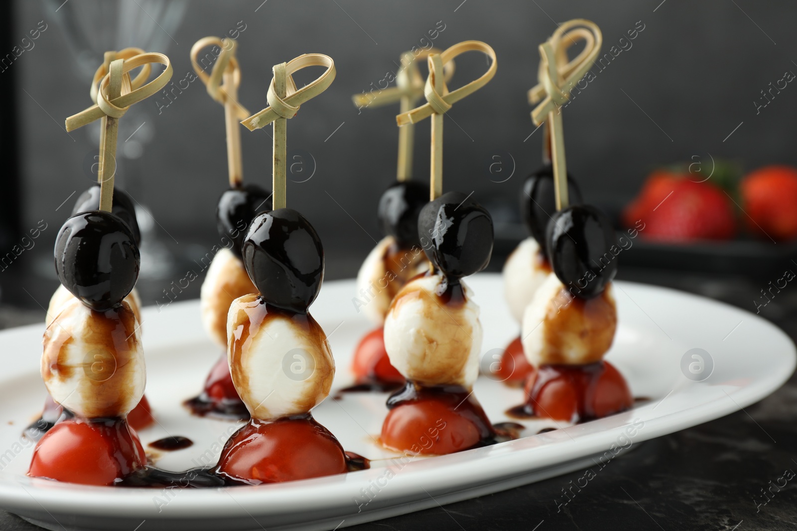 Photo of Tasty canapes with black olives, mozzarella and cherry tomatoes on dark textured table, closeup