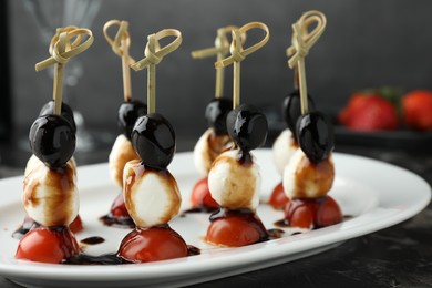 Tasty canapes with black olives, mozzarella and cherry tomatoes on dark textured table, closeup