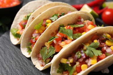 Photo of Tasty tacos with vegetables on black table, closeup