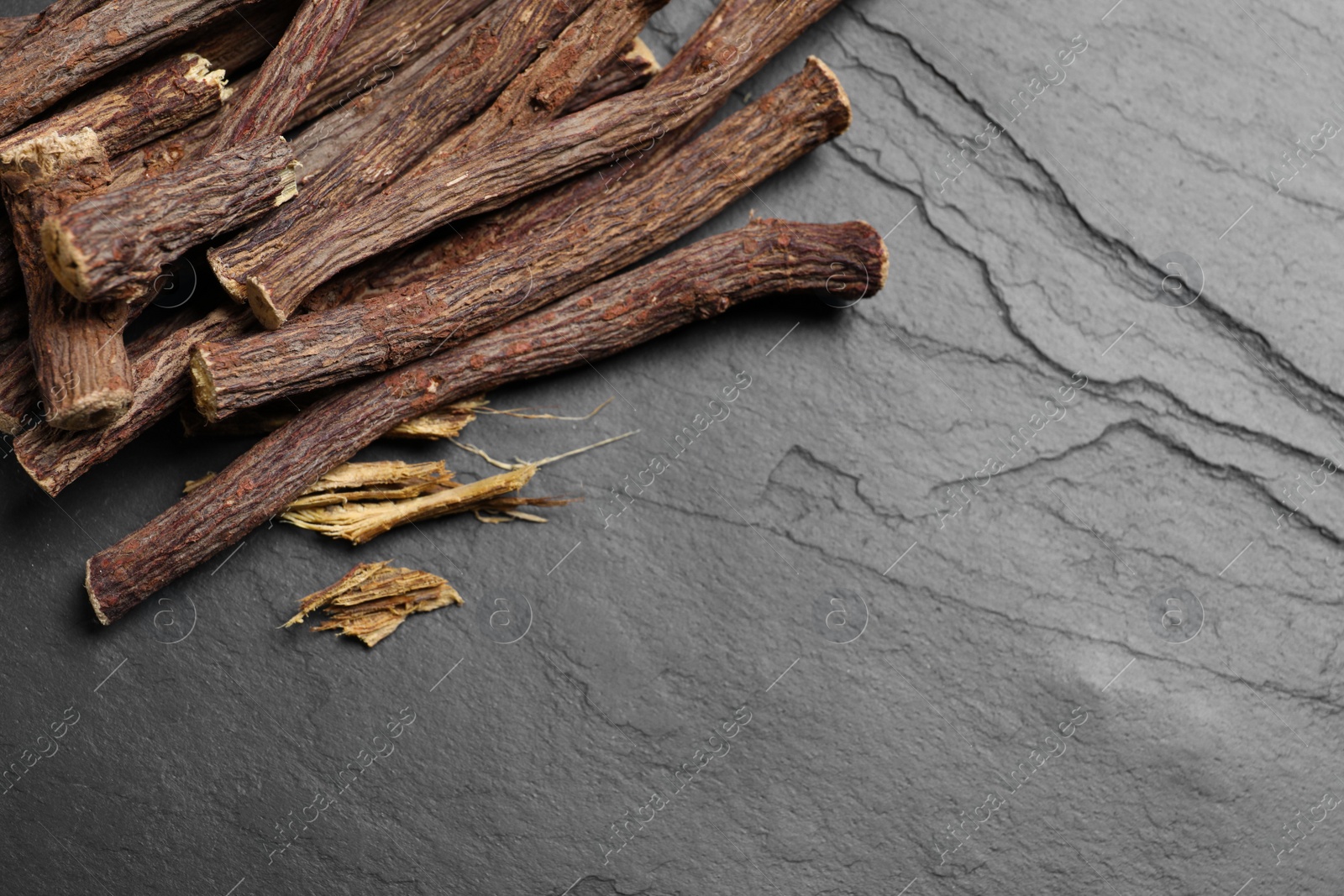 Photo of Dried sticks of liquorice root on black table, flat lay. Space for text