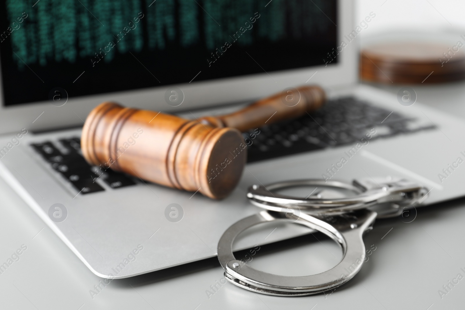 Photo of Laptop, wooden gavel and handcuffs on light table, closeup. Cyber crime