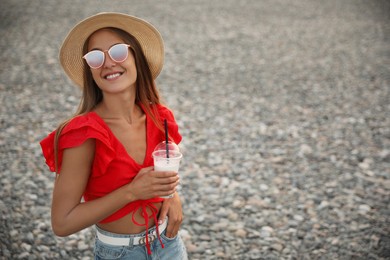Photo of Beautiful young woman with tasty milk shake on beach, space for text