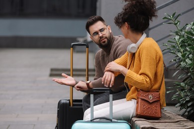 Photo of Being late. Woman and man with suitcases sitting on bench outdoors, space for text