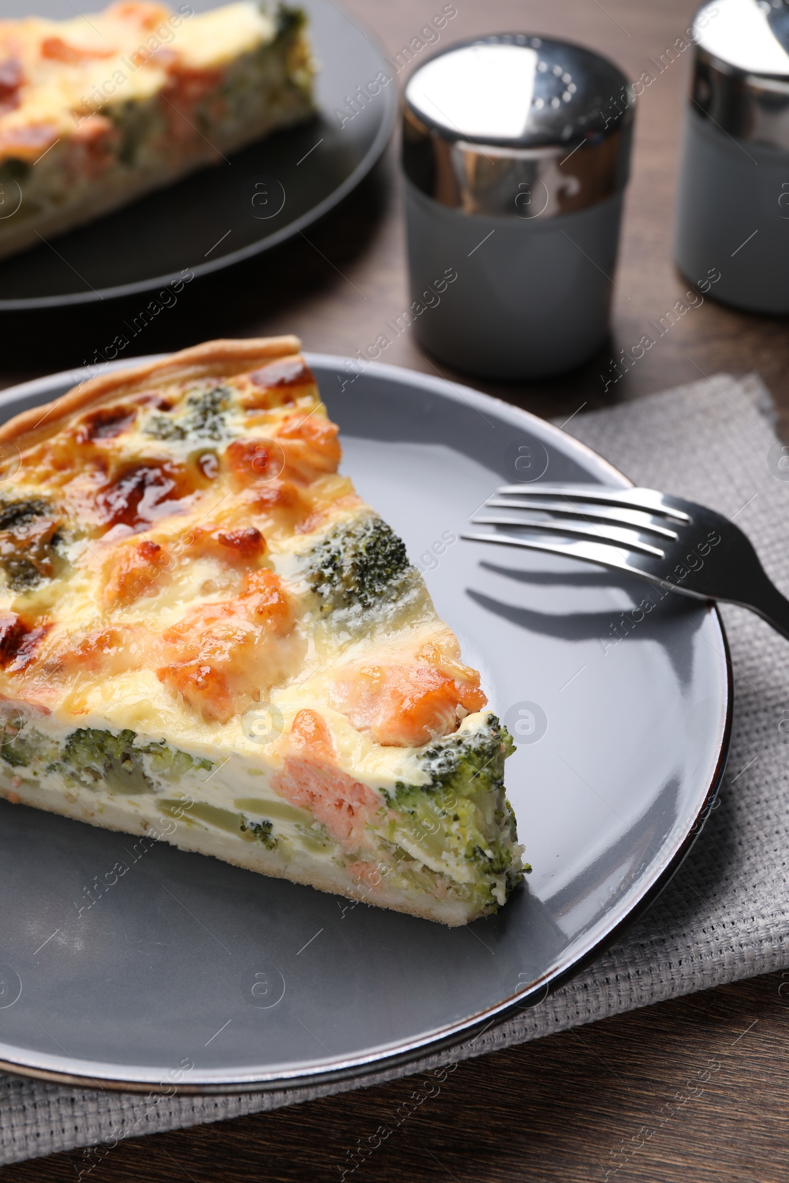 Photo of Piece of delicious homemade salmon quiche with broccoli and fork on wooden table