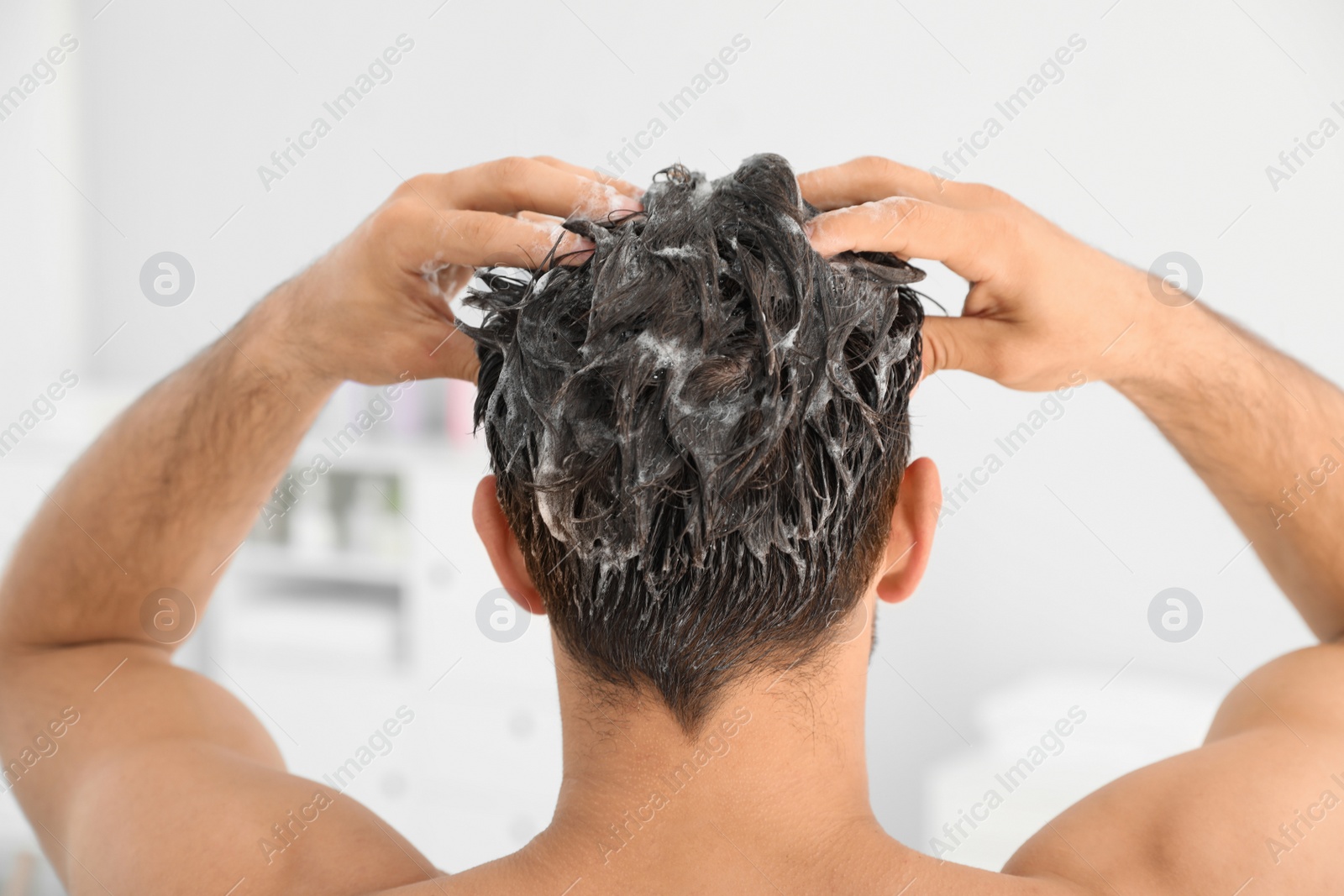Photo of Man applying shampoo onto his hair against light background
