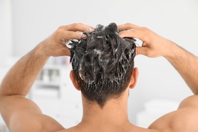Photo of Man applying shampoo onto his hair against light background