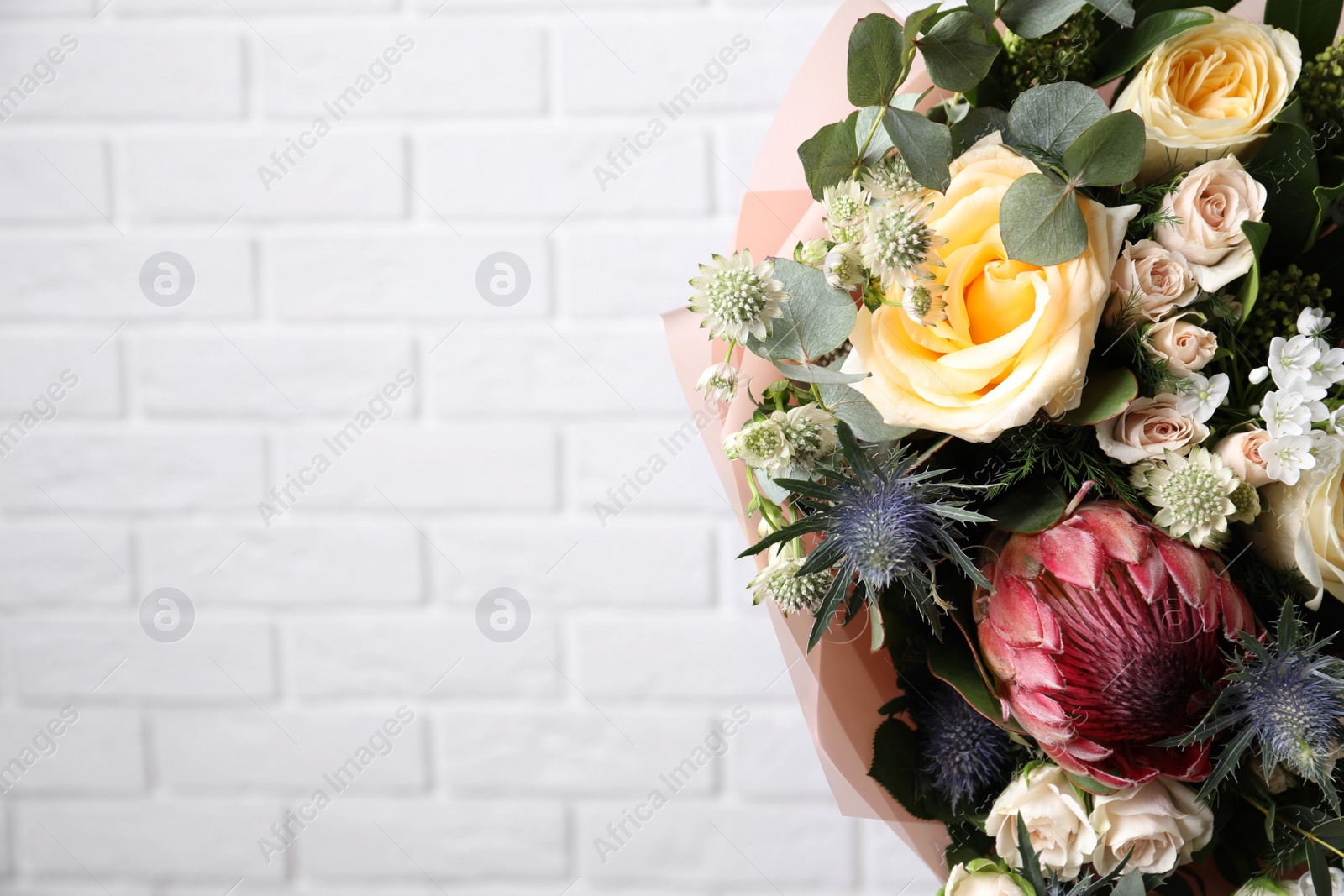 Photo of Beautiful bouquet with roses near white brick wall, closeup. Space for text