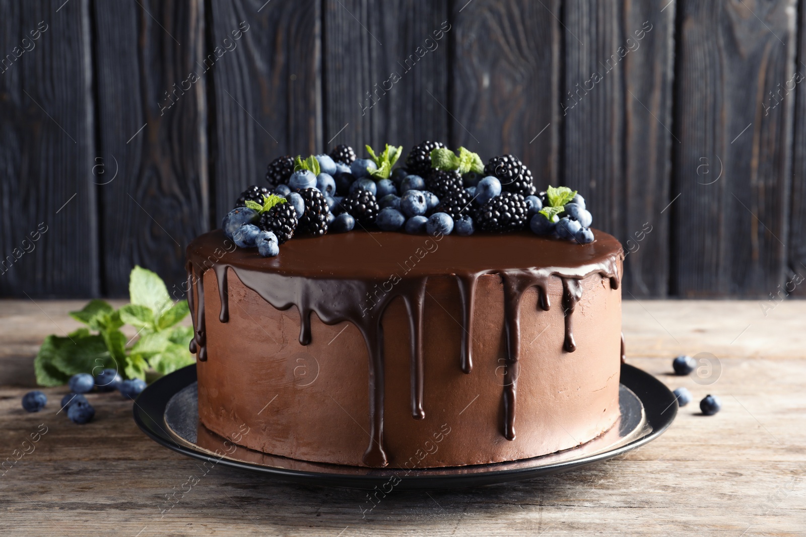 Photo of Fresh delicious homemade chocolate cake with berries on table against wooden background