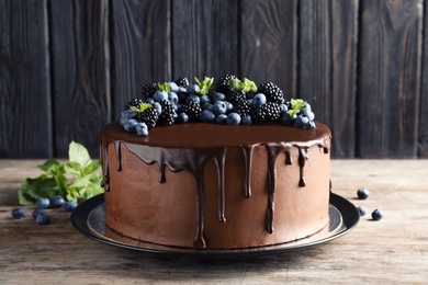 Photo of Fresh delicious homemade chocolate cake with berries on table against wooden background