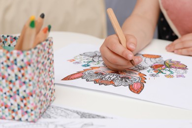 Photo of Little girl coloring antistress page at table, closeup