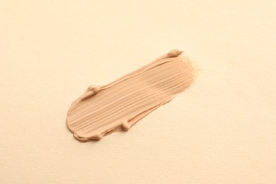 Photo of Smear of skin foundation on beige background, top view