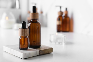 Photo of Bottles of essential oil on white countertop in bathroom, closeup. Space for text