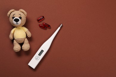 Photo of Toy bear, thermometer and pills on brown background, flat lay. Space for text
