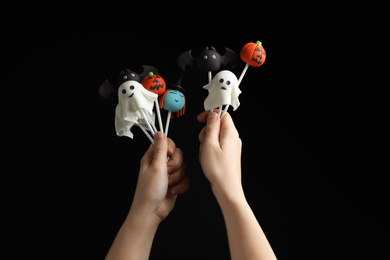 Photo of Woman with delicious cake pops on black background, closeup. Halloween celebration