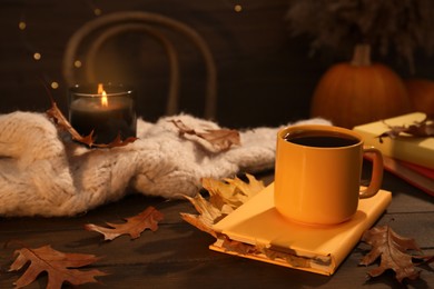 Cup of aromatic tea, book and autumn leaves on wooden table indoors