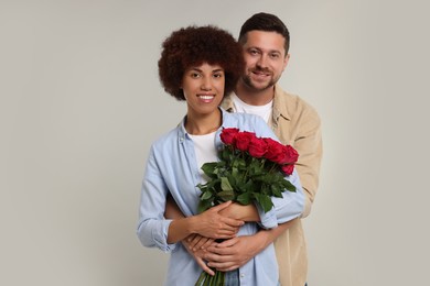 International dating. Happy couple with bouquet of roses on light grey background