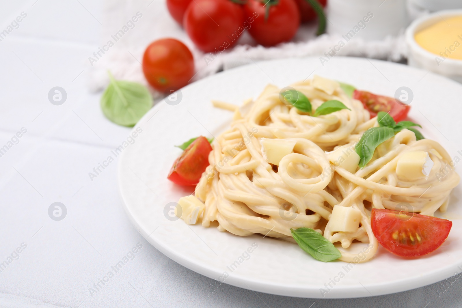 Photo of Delicious pasta with brie cheese, tomatoes and basil leaves on white tiled table, closeup. Space for text