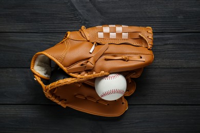 Photo of Catcher's mitt and baseball ball on black wooden table, top view. Sports game