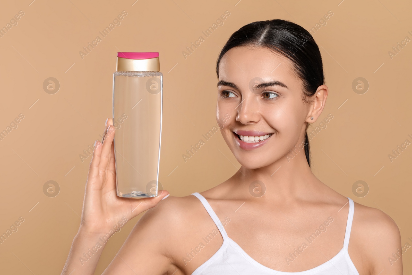 Photo of Young woman with bottle of micellar water on beige background