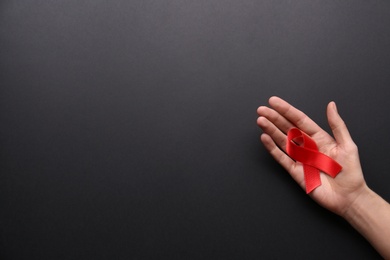 Woman holding red awareness ribbon on black background, top view with space for text. World AIDS disease day