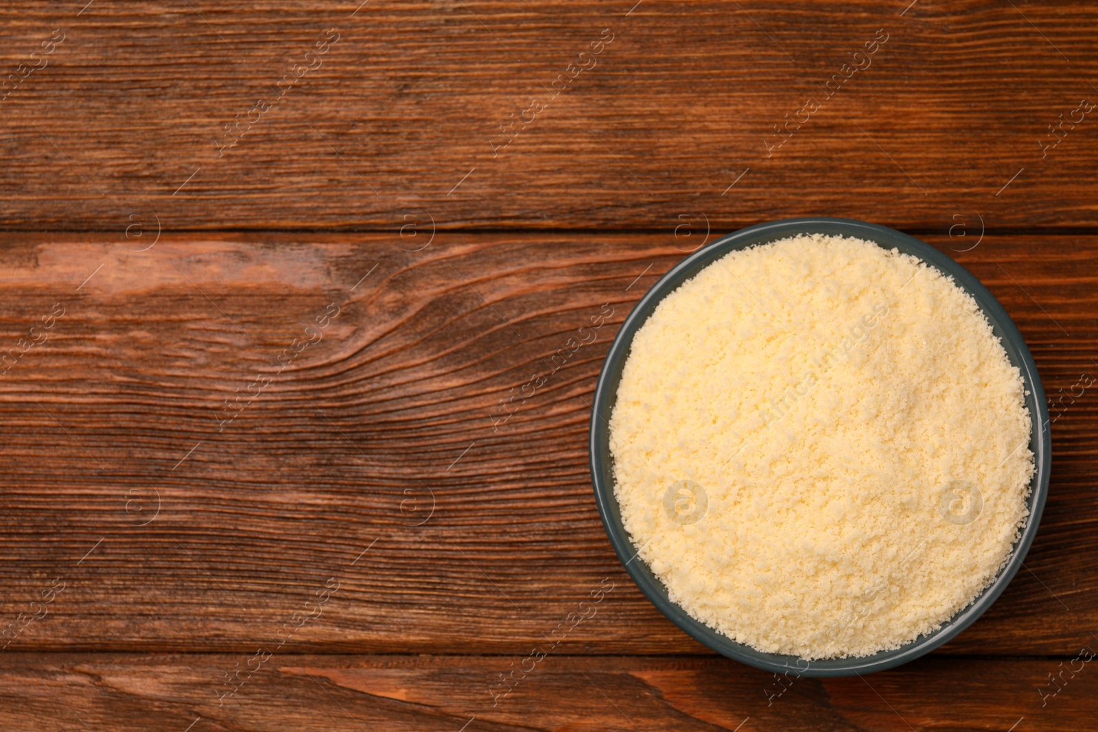 Photo of Delicious grated parmesan cheese in bowl on wooden table, top view. Space for text