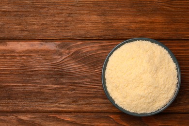 Photo of Delicious grated parmesan cheese in bowl on wooden table, top view. Space for text