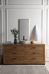 Modern bathroom interior with stylish mirror, eucalyptus branches, vessel sink and wooden vanity