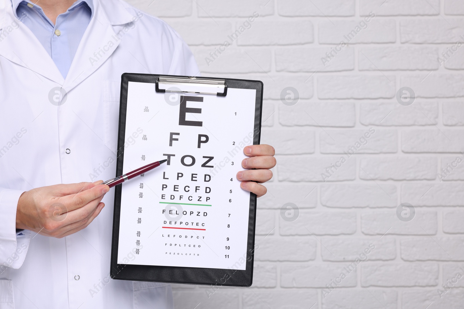 Photo of Ophthalmologist pointing at vision test chart near white brick wall, closeup. Space for text