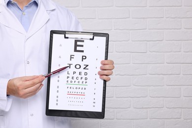 Ophthalmologist pointing at vision test chart near white brick wall, closeup. Space for text