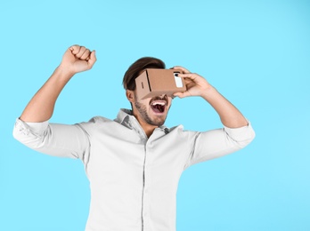 Young man using cardboard virtual reality headset on color background